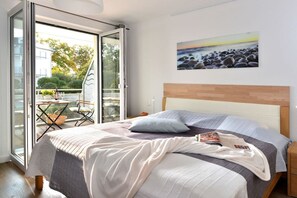 Een slaapkamer met een bed, een nachtkastje, een schilderij en uitzicht door een glazen deur op een buitengebied.