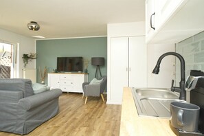 Eine moderne Küche mit integriertem Spülbecken, ein graues Sofa und ein Fernseher im Wohnbereich.