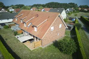 Ein zweistöckiges Haus mit geneigtem Dach, einer Holzterrasse und einem umzäunten Garten.