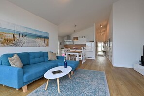 A modern living room with a blue sofa, a white coffee table, and a beach-themed painting on the wall. - Holiday apartment in Glowe with swimming pool (Glowe)