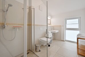 Et moderne badeværelse med en glasvægs bruseniche, toilet, vask og et vindue med naturligt lys.