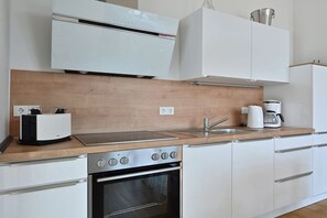 A modern kitchen with a built-in oven, a toaster, a coffee maker, and white cabinetry. - Holiday apartment in Glowe with swimming pool (Glowe)