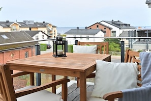 En træterrasse med et bord og stole, med udsigt over et boligområde med huse og et vandareal.