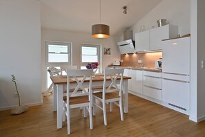 Et moderne køkken med hvide skabe, et træspisebord og en hængende lampe.