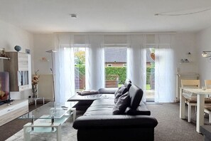 Ein modernes Wohnzimmer mit einer Couch, einem Glastisch und einem Essbereich mit Tisch und Stühlen.