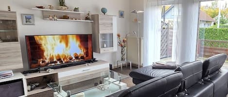 Moderni olohuone, jossa on litteänäyttöinen televisio, musta nahkasohva, lasinen sohvapöytä ja takka.