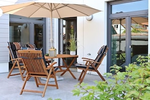 Ein Sitzbereich im Freien mit Holzkästen und einem Tisch, einer Topfpflanze und einem großen Sonnenschirm.