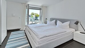 Ein modernes Hotelzimmer mit einem großen Bett, einem Nachttisch, einer Lampe und Blick ins Freie.