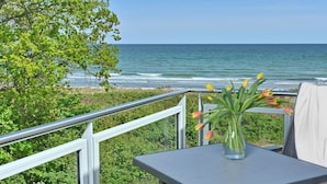 Ein Balkon mit Blick auf den Ozean, ein Glastisch mit Blumen und ein Metallgeländer.