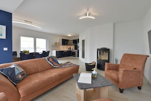 A modern living room with a sofa, armchair, and a small table. There is a kitchen in the background with cabinets and a stove. - Holiday home with 3 bedrooms (Breege\/ Juliusruh OT Breege)