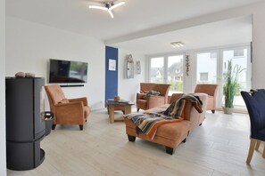 A modern living room with a fireplace, sofas, a TV, and large windows. - Holiday home with 3 bedrooms (Breege\/ Juliusruh OT Breege)