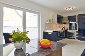 A modern kitchen with a glass dining table, a vase with flowers, and a fruit basket. - Holiday home with 3 bedrooms (Breege\/ Juliusruh OT Breege)
