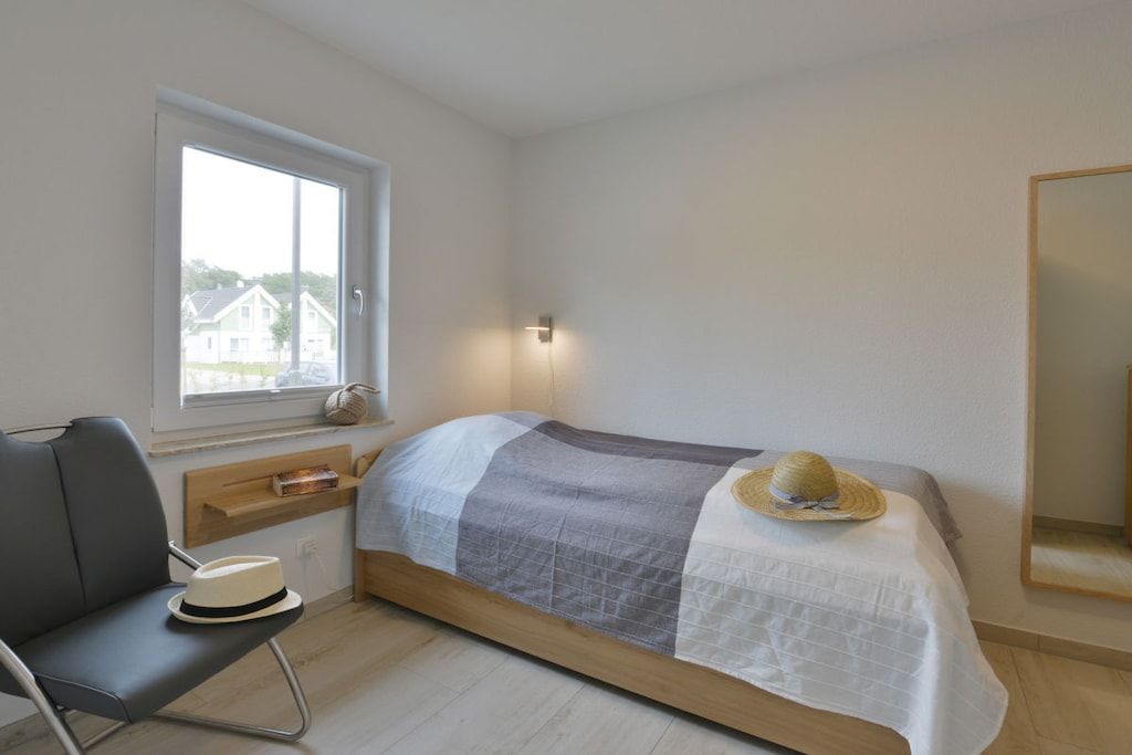 A bedroom with a bed, a chair, a window, and a mirror.