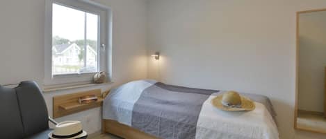 Un dormitorio con cama, una silla, un ventanal y un espejo.