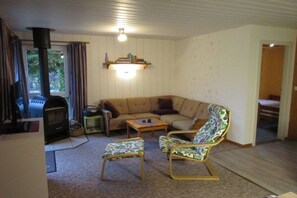 Ein gemütliches Wohnzimmer mit einer Couch, zwei gemusterten Sesseln, einem kleinen Tisch, einem Kamin und einem Bücherregal.