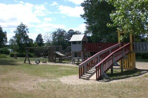 A playground with a wooden climbing structure, a slide, and a red staircase. - Holiday home in Granzow with swimming pool (Granzow)