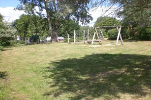 An outdoor area with a swing set, trees, and a grassy field. - Holiday home in Granzow with swimming pool (Granzow)