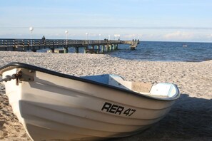 Ein kleines Boot mit dem Kennzeichen 'RE 47' an einem sandigen Strand, im Hintergrund ein Steg.