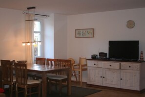 Ein Essbereich mit einem Holztisch und Stühlen, einem Fernseher auf einem Schrank und einer Uhr an der Wand.