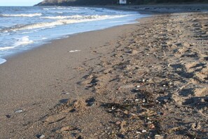 Una spiaggia con impronte e conchiglie, un cielo sereno e un promontorio in lontananza.