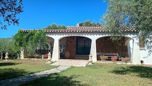 Eine Villa mit Ziegeldach, einem Steinweg, der zum Eingang führt, und Kübelpflanzen rund um die Terrasse.