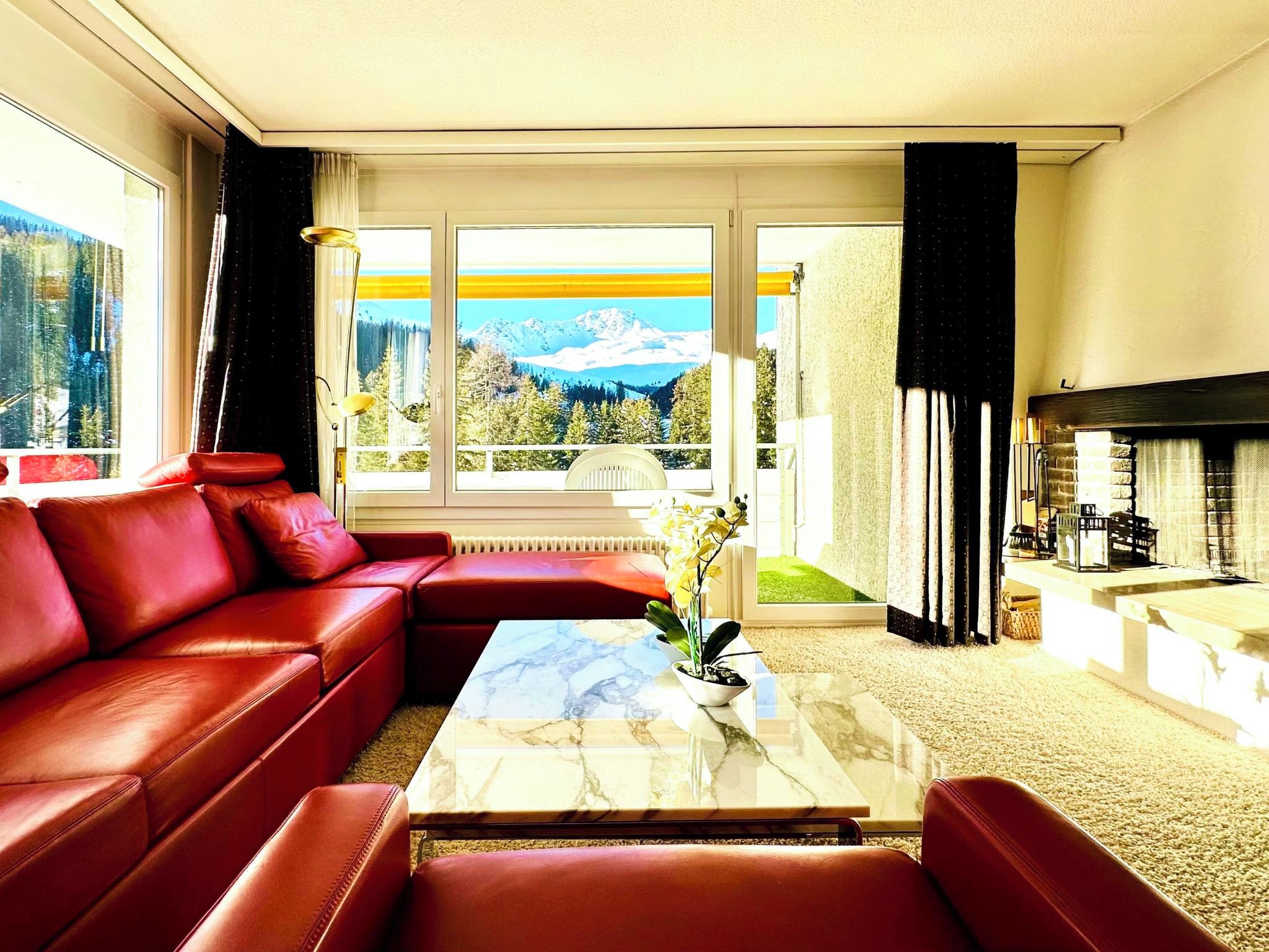 Ein Wohnzimmer mit einem roten Ledersofa, einem Marmortisch und Bergblick durch große Fenster.