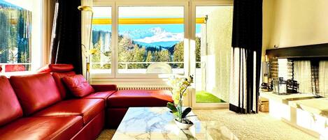 Ein Wohnzimmer mit einem roten Ledersofa, einem Marmortisch und Bergblick durch große Fenster.