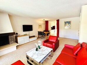 Een woonkamer met een open haard, een flatscreen televisie, een eethoek en rode meubels.