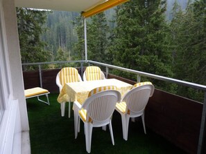 Ein Balkon mit Tisch und Stühlen, umgeben von einer Holzterrasse und Blick auf einen Wald.