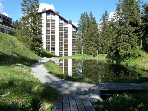 Een meerlaags hotel met een spiegelbeeld in een vijver, omgeven door groen en bomen.