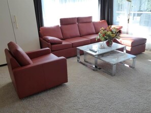Een moderne woonkamer met een rode zithoek, een glazen salontafel en een vaas met bloemen.