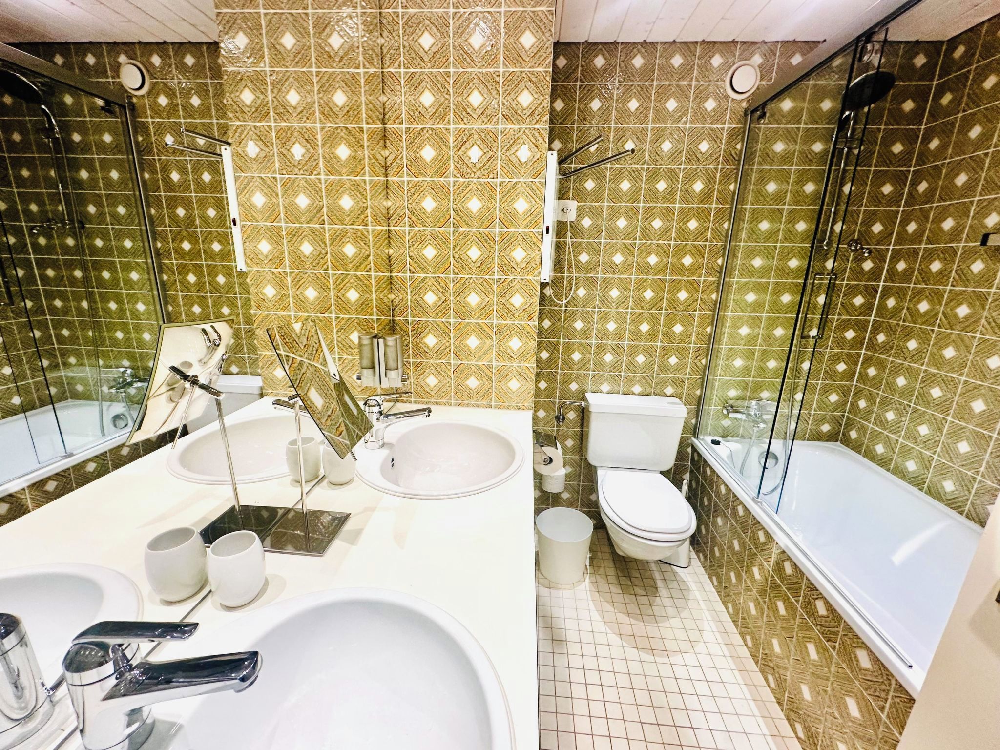 Une salle de bain avec un grand lavabo, deux miroirs, des toilettes et une baignoire.