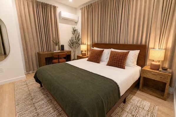 A hotel room with a bed, bedside tables, a desk, and a mirror.