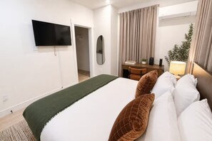 A hotel room with a bed, a TV mounted on the wall, a desk with a chair, a lamp, and a plant. - King Bed-Unbeatable Location-Bishop Arts- Unit 4 (Dallas)