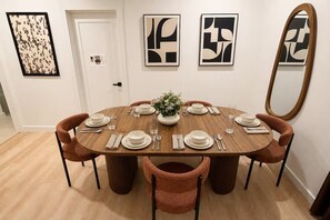 A dining room with a round table set for six, surrounded by six chairs, with abstract art on the walls and a mirror on the right.
