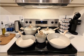 A kitchen with a stove, pots, pans, and a coffee maker.