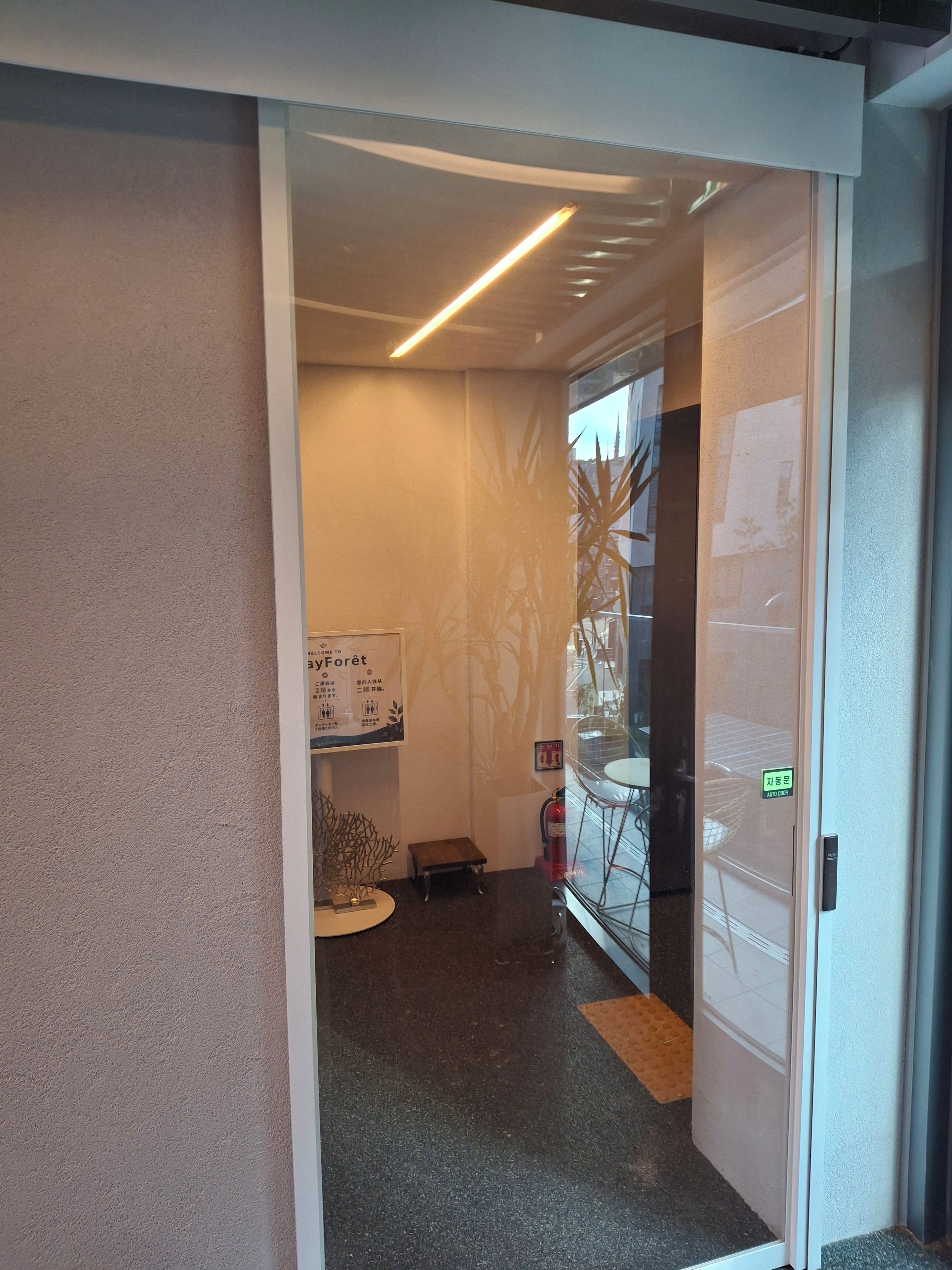An interior view of a hotel lobby with a reception desk, a small seating area, and a fire extinguisher.