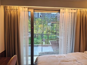 Une chambre d’hôtel avec un lit, une chaise, une vue sur un balcon et un paysage urbain en arrière-plan.