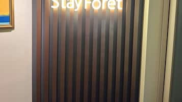 Uma área de recepção com parede listrada verticalmente e um letreiro que diz 'Stay Forêt'.