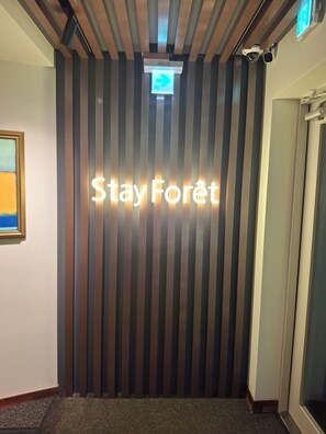 Uma área de recepção com parede listrada verticalmente e um letreiro que diz 'Stay Forêt'.
