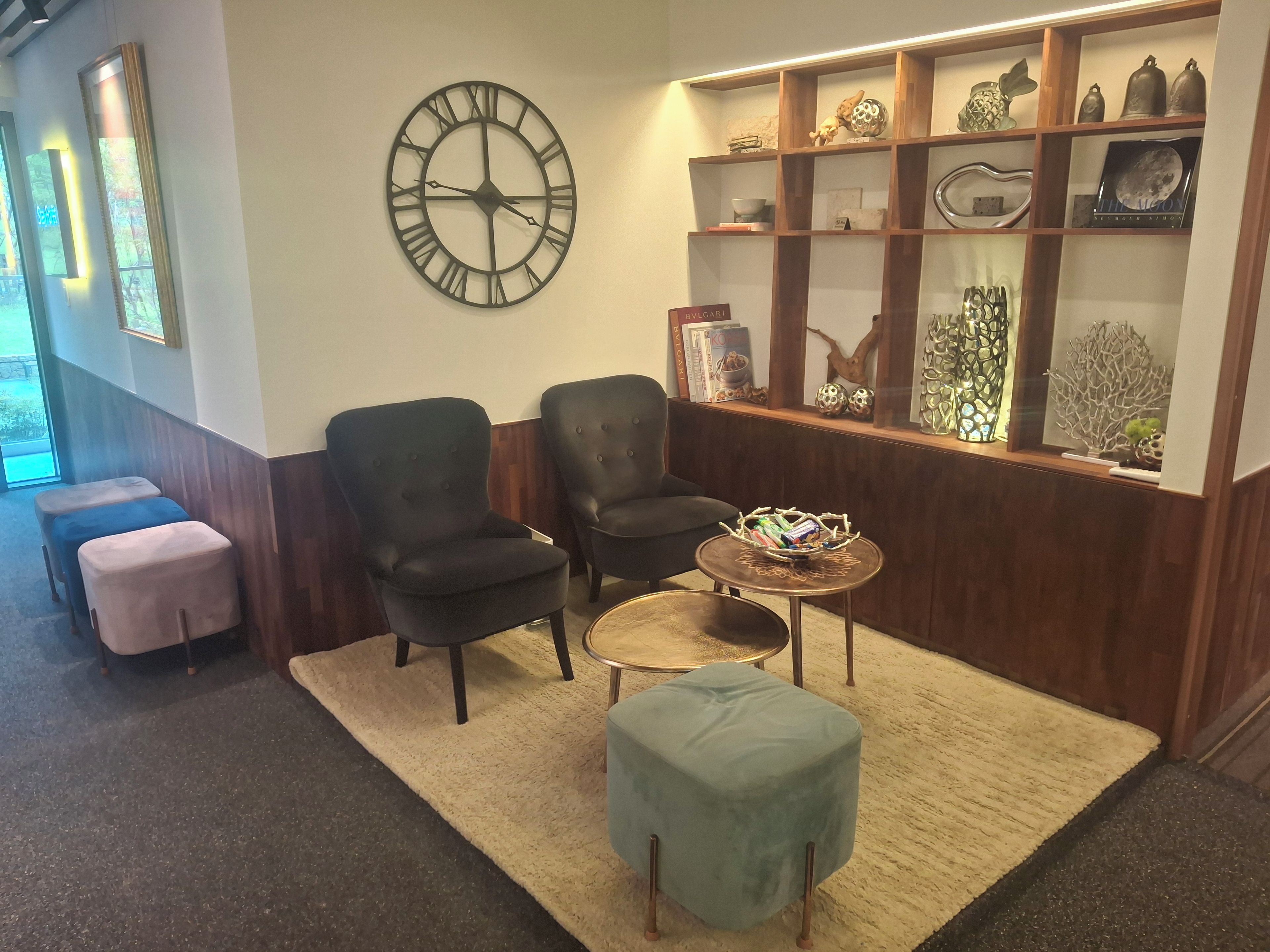 A lobby with two armchairs, a round table with a basket, a clock, and a shelf with decorative items.