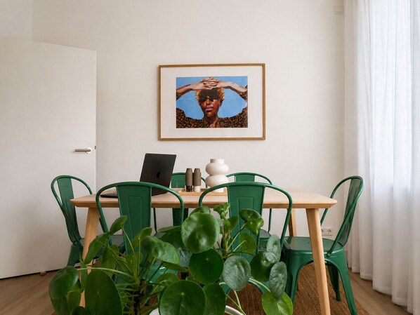 Zona de dinar amb taula, cadires, un ordinador portàtil, un quadre emmarcat i una planta en test.