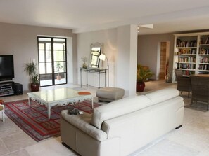 Ein Wohnzimmer mit einem weißen Sofa, einem Couchtisch, einem Fernseher, einem Bücherregal und einem großen Fenster.