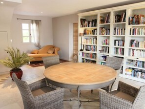 Ein Wohnzimmer mit einem runden Tisch, vier Korbstühlen, einer Couch, einem Bücherregal und einem Blumentopf.