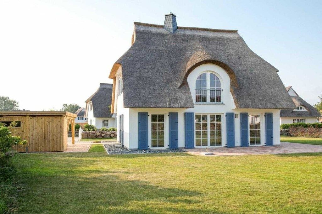 Une maison avec un toit à forte pente, une grande fenêtre en arc de cercle et une pelouse bien entretenue.