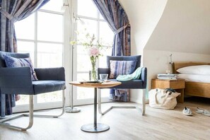 A hotel room with a bed, two armchairs, a small round table, and a window with curtains. - Holiday home Reed Warbler 43 (Fuhlendorf)