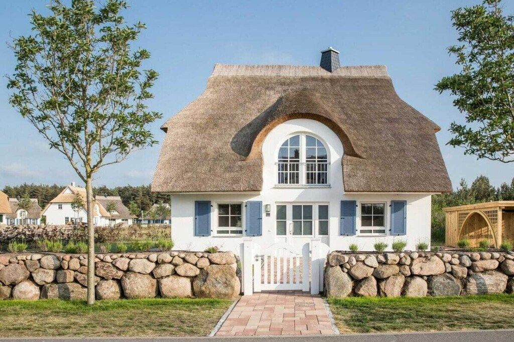 A house with a thatched roof, white exterior walls, and a stone wall surrounding the property.