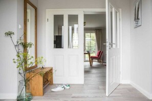 A hallway with a white door, a wooden console table, a vase with green foliage, and a pair of white sneakers on the floor. - Holiday home with 1 bedroom (Fuhlendorf)