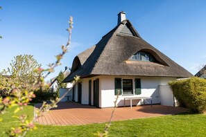 A thatched-roof house with a wooden deck and a white exterior. - Holiday home with 1 bedroom (Fuhlendorf)