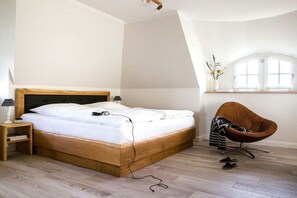 A bedroom with a wooden bed, a bedside table, a chair, and a window with a view. - Holiday home with 1 bedroom (Fuhlendorf)